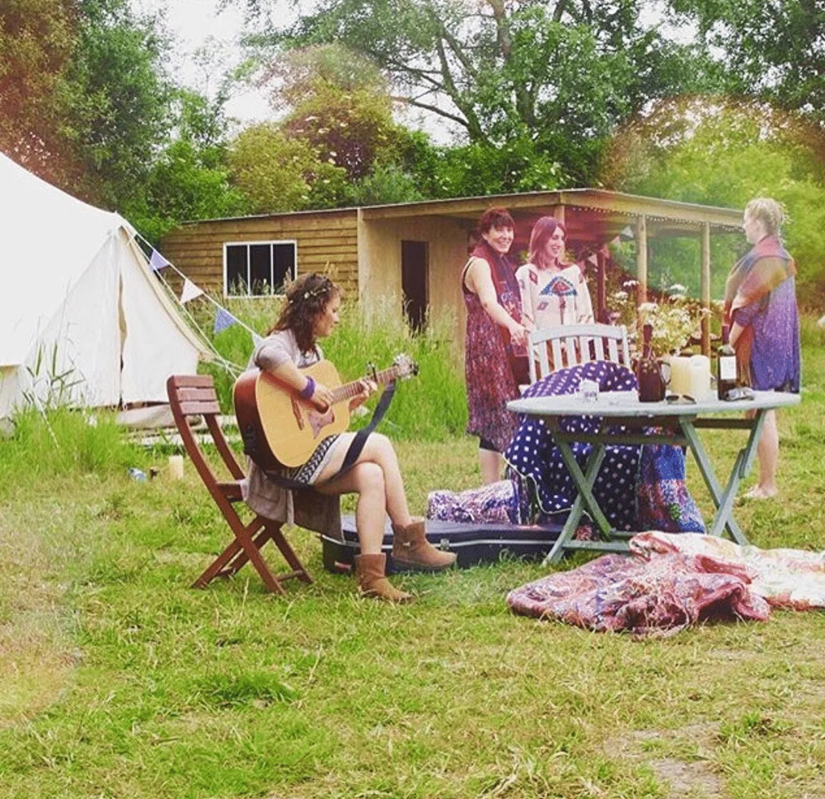 Friends relaxing with a guitar by the shelter and bell tent at Chalke Valley