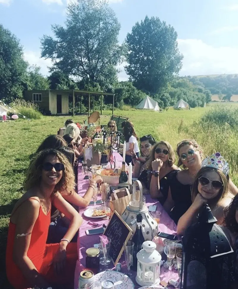 Friends having a meal outside at a long table with bell tents visible