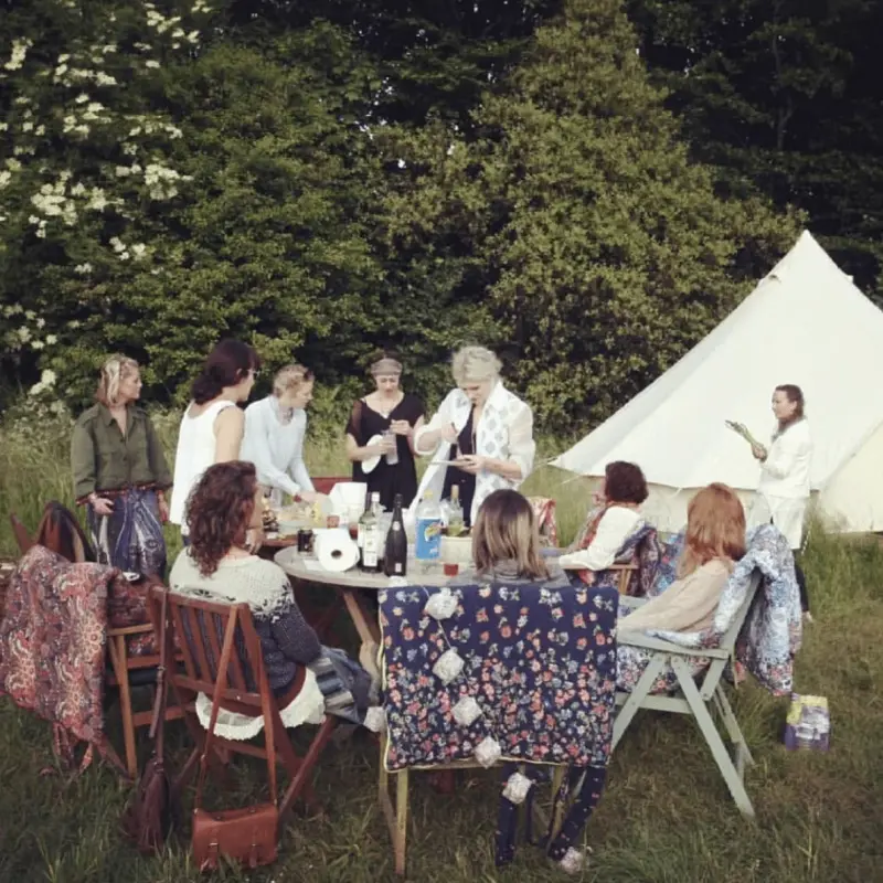Friends gathered around a table with a bell tent in the background at Chalke Valley