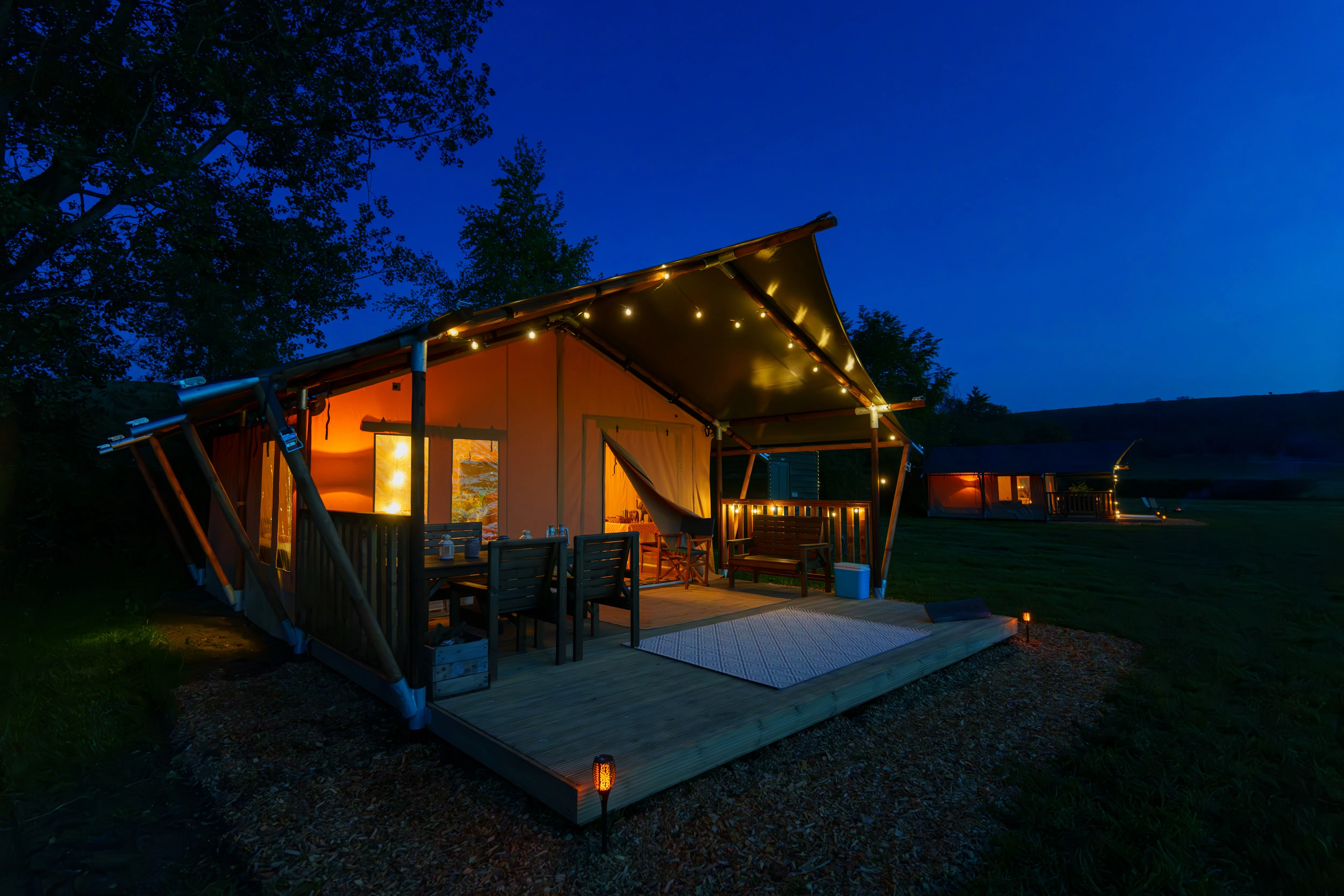Safari tent deck with festoon lights at nightfall at Chalke Valley Camping