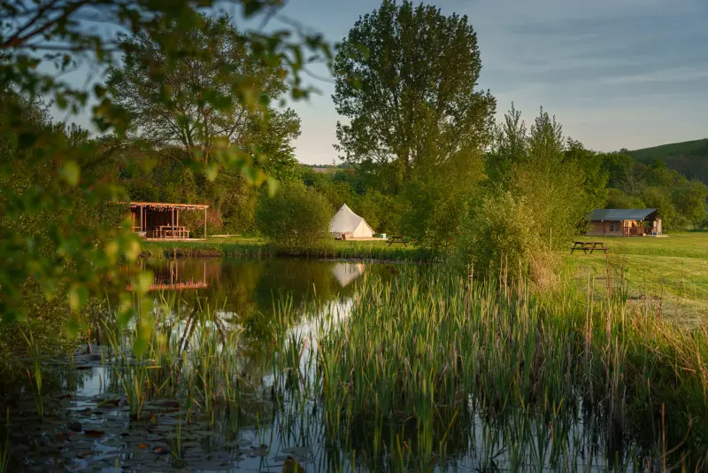 Pond in daylight with safari tent, bell tent and shelter at Chalke Valley