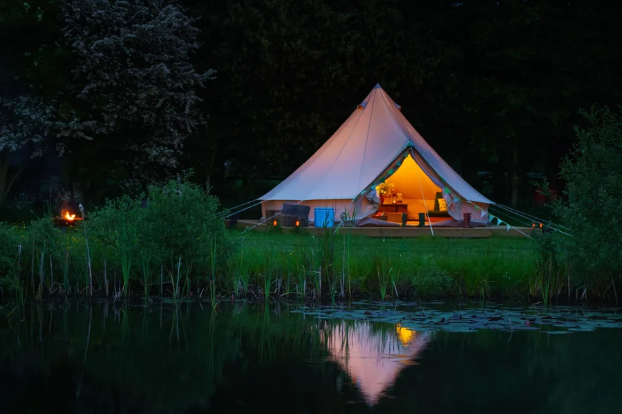 Bell tent lit up at dusk with view over the pond at Chalke Valley Camping