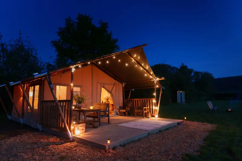 Safari tent exterior at dusk with lights at Chalke Valley Camping
