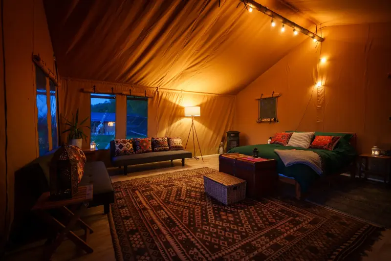 Interior of a safari tent with bed, sofas and lamp at Chalke Valley Camping